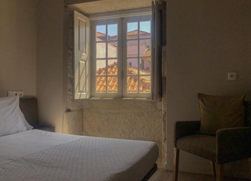 a bedroom with a bed and a window with a chair at Rua Grande Hotel in Viana do Castelo