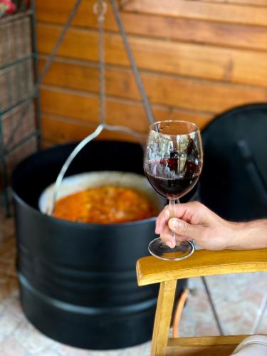 a person holding a glass of wine next to a pot of chili at Panoráma Faház Mohács in Mohács