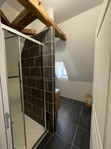 a bathroom with a glass shower and black tiles at La loge d’Evelyne in Villecomtal