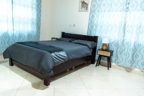 a bedroom with a bed with blue curtains and a table at Lovely 4 Bedroom Solar Powered House with CCTV and Unlimited WiFi near Devtraco Court Community 25 Tema in Tema