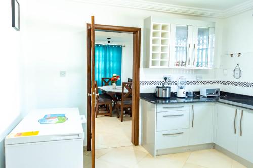 a kitchen with white cabinets and a dining room at Lovely 4 Bedroom Solar Powered House with CCTV and Unlimited WiFi near Devtraco Court Community 25 Tema in Tema