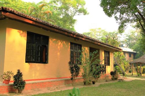 a yellow house with windows and trees in front of it at Green Mansions Jungle Resort in Sauraha