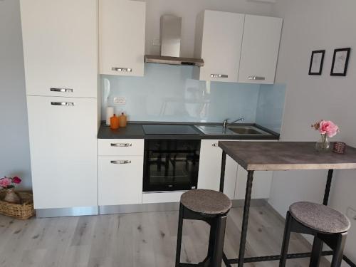 a kitchen with white cabinets and a table and stools at Apartma ODDIH in Dutovlje
