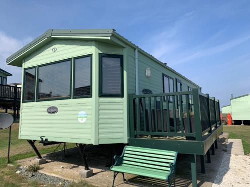 a green and white tiny house with a bench at Thornwick Bay Haven Site-Large Homely Static Caravan, Sun, Sea And Sand (SEA VEIWS , LIGHTHOUSE VEIWS) in Flamborough