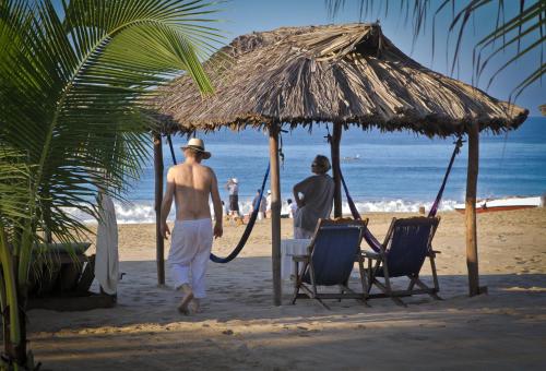 two men walking on the beach under a straw umbrella at Hotel Gilda in Coyuca