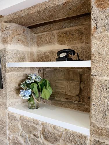 a stone fireplace with a vase of flowers on a shelf at Celanova House in Celanova