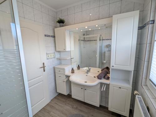 ein weißes Badezimmer mit einem Waschbecken und einem Spiegel in der Unterkunft Das Inselhaus in Norddeich