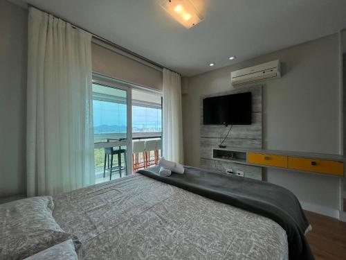 a bedroom with a bed and a television and a balcony at TR01- Suíte+1 | Vista Incrível | Piscina|Big Wheel in Balneário Camboriú