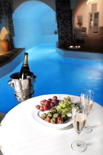 a plate of fruit and wine glasses on a table at Oia Mare Villas in Oia