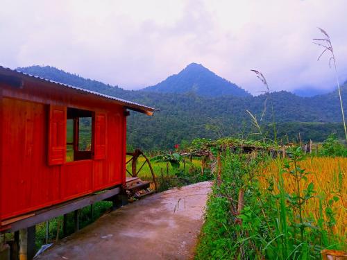 una casa rossa in un campo con una montagna sullo sfondo di ChienDe Homestay a Sa Pa