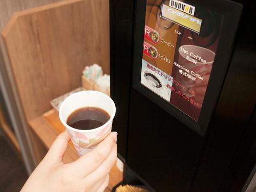 a person holding a cup of coffee in a vending machine at Hotel Route Inn Matsuyama -Katsuyama Dori- in Matsuyama
