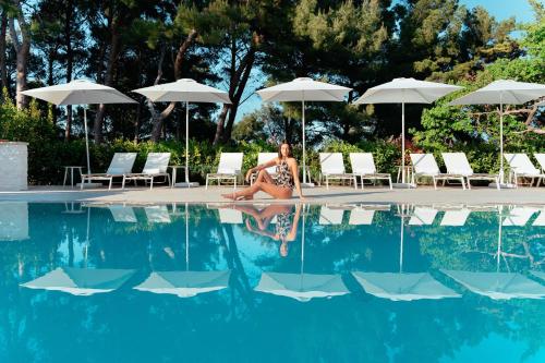 San Michele Relais & Spa في سيرولو: امرأة ترتدي البيكيني جالسة بجوار حمام السباحة