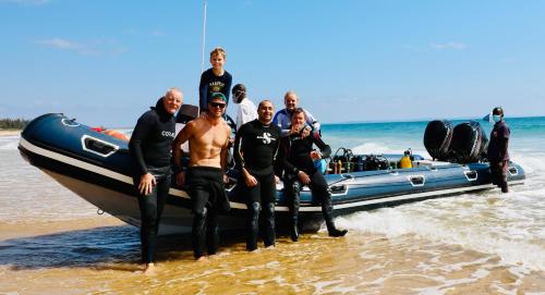 a group of men standing next to a boat on the beach at Vista do Mar in Inhambane