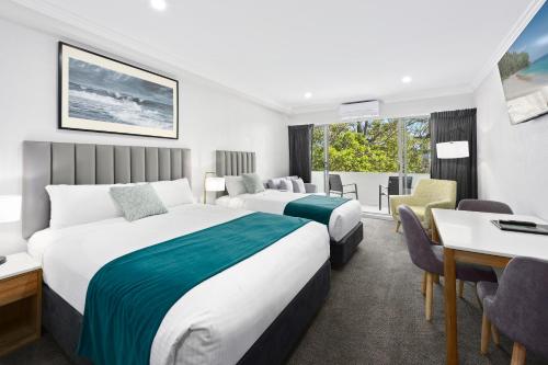 a hotel room with two beds and a desk at Palm Court Motor Inn in Port Macquarie