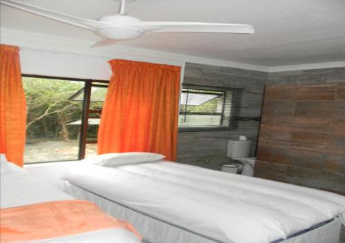 a bedroom with two beds and an orange curtain at Peace Cottages Uvongo. in Uvongo Beach