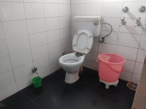 a bathroom with a toilet and a pink bucket at Hotel Shubam Banquet & Restaurant By WB Inn in Jammu