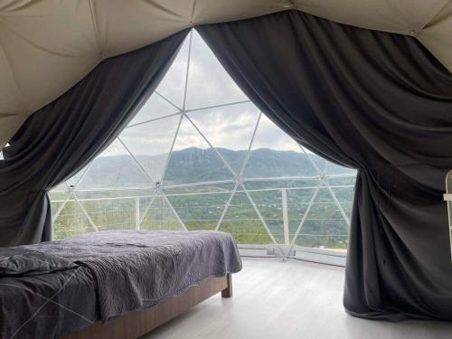 a bed in a room with a large window at 4 seasons. 4 სეზონი Glamping Georgia Racha in Ambrolauri