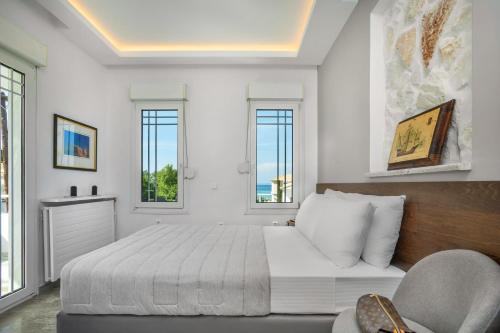 a white bedroom with a bed and two windows at Albero Villa Polychrono in Polykhrono