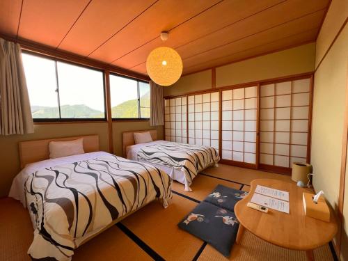 a room with two beds and a table and windows at Yufuin Hoshinosato in Yufuin