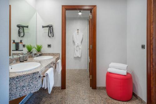 a bathroom with two sinks and a red stool at Hotel Santiago Plaza Affiliated by Meliá in Santiago de Compostela
