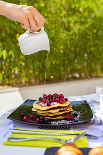 Een persoon giet stroop over een stapel pannenkoeken. bij Hotel Tiffany & Resort in Cesenatico