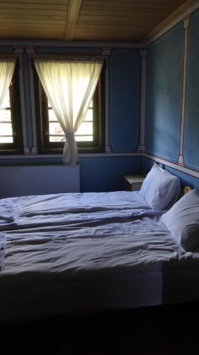 a bed in a blue room with two windows at Недкова къща in Koprivshtitsa