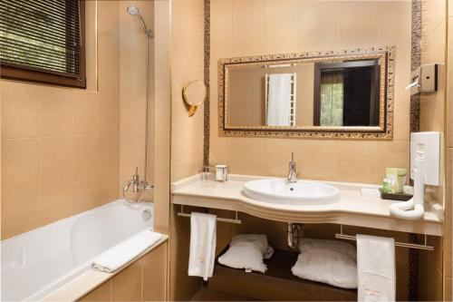 a bathroom with a sink and a tub and a mirror at Pirin Park Hotel in Sandanski