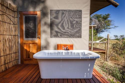 a bath tub sitting on a wooden deck with a door at Amber River Camp in Okavango Delta