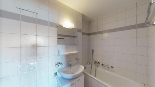 een wit betegelde badkamer met een wastafel en een bad bij Pracondu OUTDOOR & FUN appartement 8 personnes by Alpvision Résidences in Nendaz