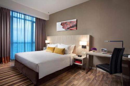 a bedroom with a bed, chair, desk and a lamp at Citadines Uplands Kuching in Kuching