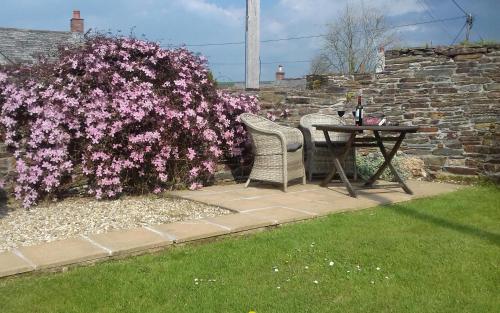 a table and chairs next to a bush with pink flowers at The Barn - Trelash, North Cornwall in Warbstow
