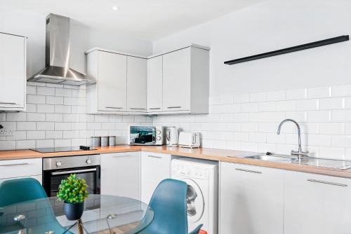 a white kitchen with a glass table and blue chairs at Cosy 2 Bed- Gillingham in Gillingham