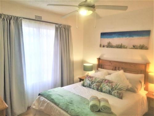 a bedroom with a bed with a ceiling fan and a window at Laguna La Crete 28 in Uvongo Beach