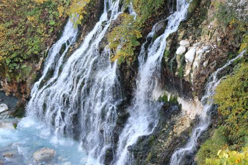 a waterfall on the side of a mountain at Biei Shirogane Onsen AONOBI YUYU in Biei