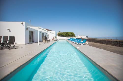 a swimming pool with blue chairs and the ocean at Casa Conil with a private 25 meter heated pool in Conil