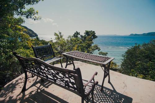 two benches sitting next to a table and the ocean at Sangat Island Dive Resort in Coron