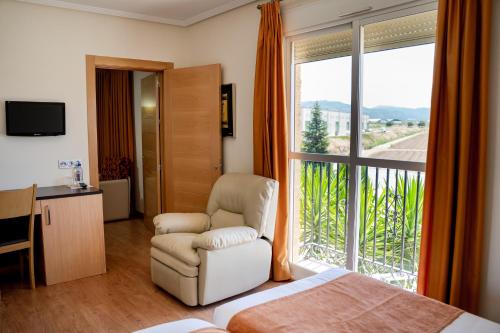 a bedroom with a bed and a chair and a window at Hotel Malena in Caravaca de la Cruz