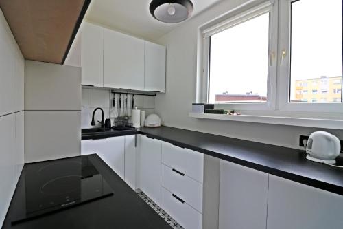 Biała kuchnia z białymi szafkami i oknem w obiekcie AAPARTAMENT w mieście Gdynia