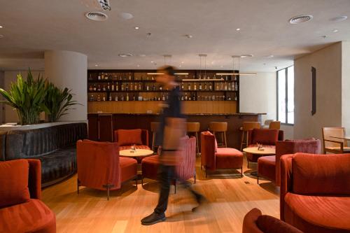 a person walking through a restaurant with tables and chairs at QOYA Hotel Curitiba, Curio Collection by Hilton in Curitiba