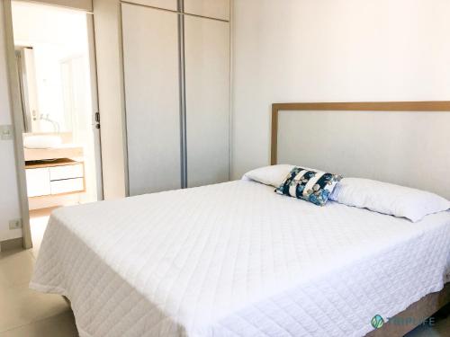 1 dormitorio con cama blanca y cabecero de madera en Apartamento da Pitangueiras, en Guarujá