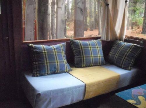 un sofá con almohadas sentado frente a una ventana en Cabaña El Deseo En El Bosque en Balneario Mar Azul