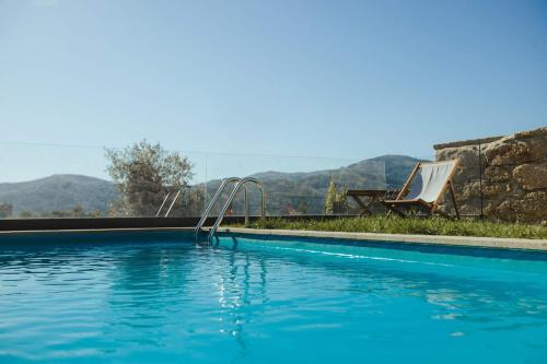 a blue swimming pool with a swing and mountains in the background at Casa da Vila - Pool & Hot Tub with Mountain View in Gerês in Terras de Bouro