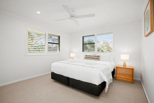 a white bedroom with a bed and two windows at Lawson Beachfront in Byron Bay