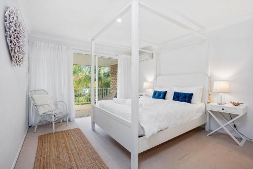 a white bedroom with a white canopy bed and a chair at Eastpoint 3 in Byron Bay