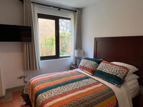 ein Schlafzimmer mit einem Bett mit einer bunten Decke und einem Fenster in der Unterkunft Cousy Condo San Rafael, 3 blocks from the parish, pool, BBQ and terrace in San Miguel de Allende