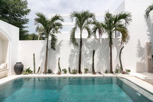 einen Pool mit Palmen vor einer weißen Wand in der Unterkunft Villa Medina Canggu in Canggu