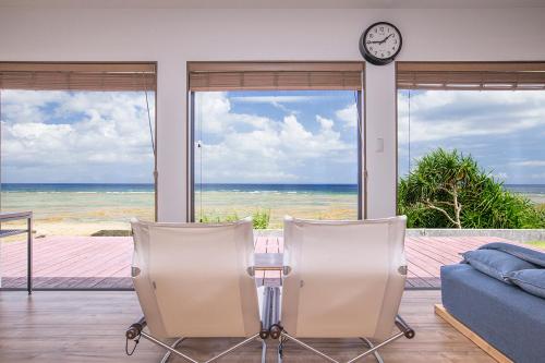a living room with a table and two chairs and a clock at ゴールデンマイルヴィラ in Amami