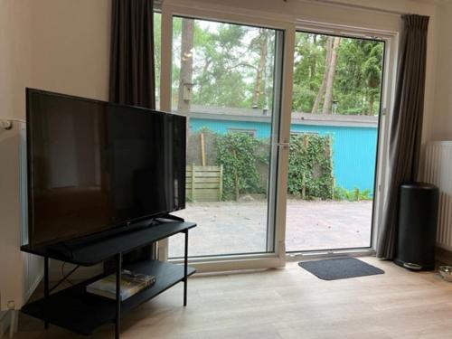 een woonkamer met een grote televisie en een grote glazen schuifdeur bij Chalet Hoenderloo in Hoenderloo