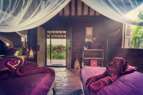 a bedroom with two beds with purple sheets and a window at Dragonfly Village in Ubud