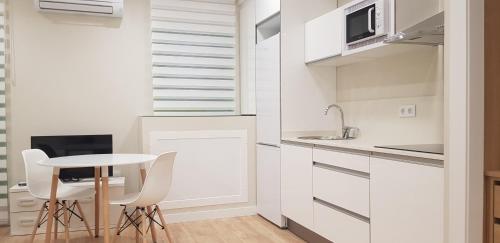 eine weiße Küche mit einem kleinen Tisch und Stühlen in der Unterkunft Apartamentos Ilustración in Albacete